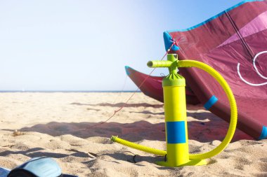 Sahilde arka planda deniz ve güneş ışığı olan uçurtma ekipmanları (pompa, uçurtma, tahta). Boşluk düşmanı metni.