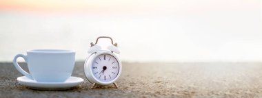 Sahilde gün doğumu. Deniz ve güneş ışığıyla taştan dalgalı suda beyaz bardak ve alarm saati. Mesaj için yer var. Güneşin doğuşu plaj kahvaltısı