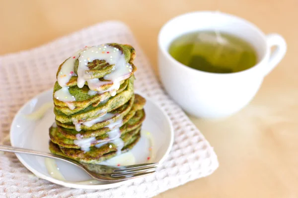 Healthy green matcha and spirulina pancakes with white vanilla sauce or condensed milk with a cup of green tea on light background. Healthy vegan breakfast with superfood