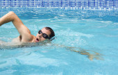 Egy férfi úszik elől a medencében úszószemüvegben. Úszni sportoló úszás medence edzés a verseny. Szakmai male watersport felnőtt edzés cardio vízben a szabadban.
