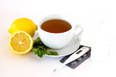 Limon, nane, termometre ve beyaz arka planda su toplayan hapların yanında beyaz bardak. Mevsimlik kış, sonbahar hastalıkları, soğuk algınlığı veya grip. Ev alternatif tedavi kavramı.