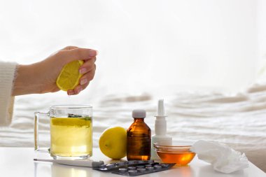 Limonlu çay hazırlayan hasta kadın. Yatak odasının arka planında bir fincan çay, limon, bal ve soğuk algınlığı ilacı olan bir masa. Alternatif tıp ve evde grip tedavisi