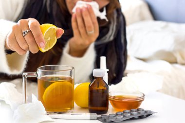 a young unrecognaseble woman with a cold or flu laying on the bed and preparing tea with lemon. Alternative medicine, home treatments and seasolan illnesses concept clipart