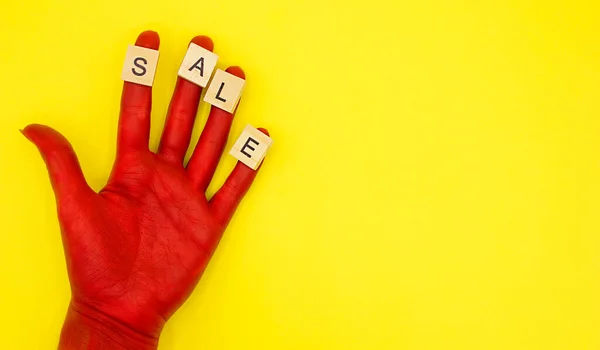 red hand with the wooden letters shaped word SALE on the fingers on a yellow background. The season of discounts and sales has begun. Space for text.