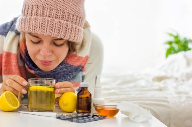 Şapka ve atkıyla sıcacık giyinmiş genç bir kadını yatağa yatırıp limonlu sıcak çay ve başka bir ilaç içerek kapat. Mevsimsel soğuk algınlığı ve hastalıklar. Ev tedavisi.