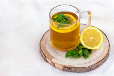 Beyaz bir zemin üzerinde ahşap tepside limonlu ve naneli bir fincan bitki çayı.