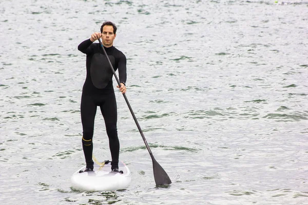 Man On Stand Up Paddle Board on the dark sea. Paddle SUP surf in winter