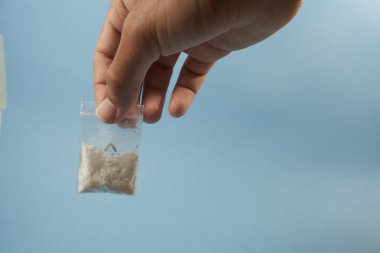 Mavi arka planda küçük bir torba kokain var.