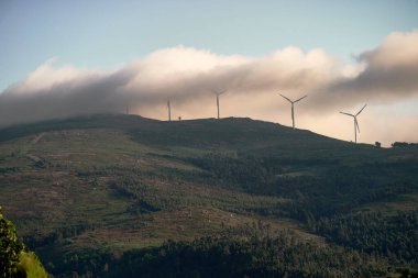 Elektrikli yel değirmenleri ve sisli yeşil dağ manzarası