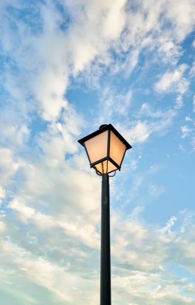 Mavi gökyüzünde turuncu ışık ve bulutlu siyah lamba direği