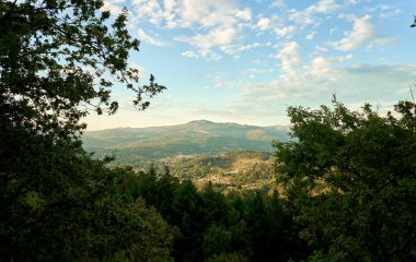 Dağlar, bitki örtüsüyle mavi gökyüzü ve altın saatinde bulutlarla kaplı.