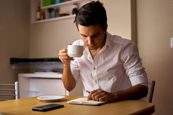 Siyah saçlı çocuk deftere not alıyor ve kahve içiyor. Ergen, ahşap masada bir şeyler çizip içiyor. Beyaz kupasını kullanarak düşünen ve yazan bir adam..