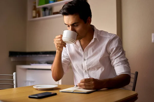 Siyah saçlı çocuk deftere not alıyor ve kahve içiyor. Ergen, ahşap masada bir şeyler çizip içiyor. Beyaz kupasını kullanarak düşünen ve yazan bir adam..