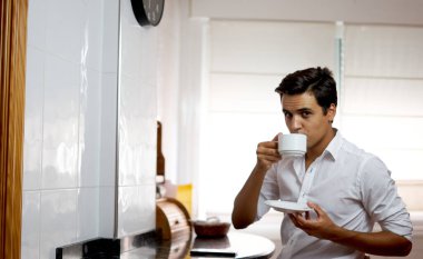 Çocuk kahve içiyor ve cep telefonunu izliyor. Tek başına kahve içen ve gülerken sosyal medyayı izleyen bir adam. Mutfakta beyaz gömlekli bir genç. Çay içerken gülen kişi