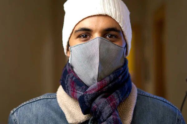 warm boy with mask. teenager in blue and red scarf with cloth mask and white wool cap. Young man in denim jacket and shearling. Sheltered person in pandemic.