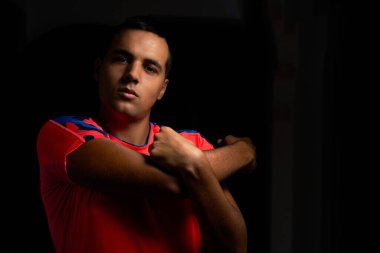 Kaslı genç adam omuz ve sırt geriyor. Turuncu spor gömlek ve siyah arka plan giyen kaslı genç çocuk. Siyah arka plandaki koyu saçlı genç adam. Kısa saçlı sporcu.