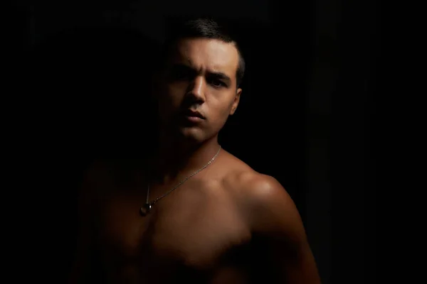 Önüne bakan kaslı genç adam. Siyah arka planda gömleksiz, kaslı bir genç. Siyah arka planda genç, üstsüz esmer. Gömleksiz sporcu ve kolyeli kısa saçlı..