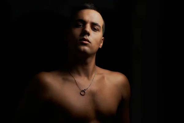 Önüne bakan kaslı genç adam. Siyah arka planda gömleksiz, kaslı bir genç. Siyah arka planda genç, üstsüz esmer. Gömleksiz sporcu ve kolyeli kısa saçlı..