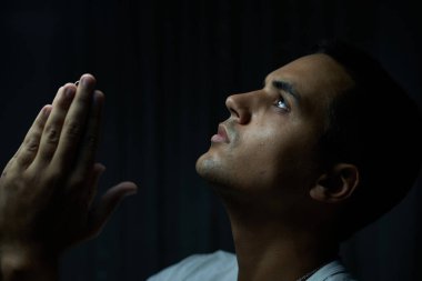 Siyah arka planda beyaz tişörtlü esmer çocuk dua ediyor. Ergen, Tanrı 'ya ciddi bakışlar ve alçak ışıkla bakıyor. Gümüş kolyeli bir adam ciddi bir ifadeyle yalvarıyor.