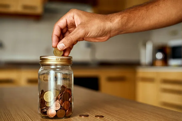 hand putting euro cent coins into a glass piggy bank. glass jar full of euro coins and golden lid. Person saving. hand with coins with blur background