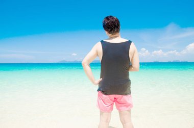 mavi deniz arka plan üzerinde siyah yelek ve pembe şort ile adam arka