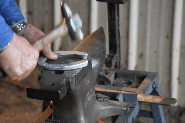 Farrier beating a horseshoe into shape on an anvil.