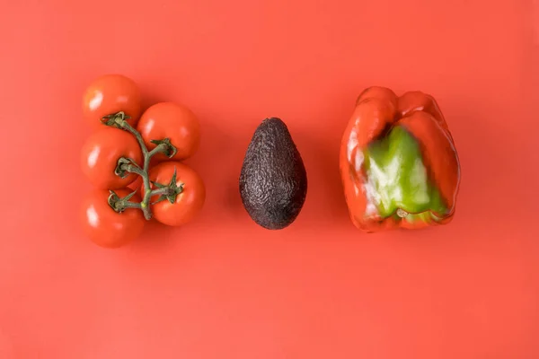 Elrendezés avokádóból, paradicsomból és borsból. Étel koncepció. Zöldségek piros háttérrel. Minimális nyári koncepció. Növényi tervezés. — Stock Fotó
