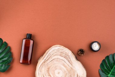 Kahverengi losyon, krem, ahşap kesitte şampuan kahverengi yüzeyde canavar yapraklarıyla kesilmiş. Kozmetik ürünler için vitrin. Kozmetik ve güzellik kavramı.