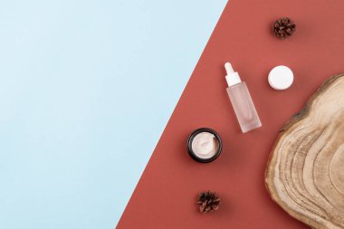 Cilt bakım ürünleri. Açık krema kavanozu, peptitli serum, ahşap kesim, kahverengi ve mavi yüzeyde çam kozalakları. Güzellik konsepti. Düz konum, düzen, kopyalama alanı, yukarıda