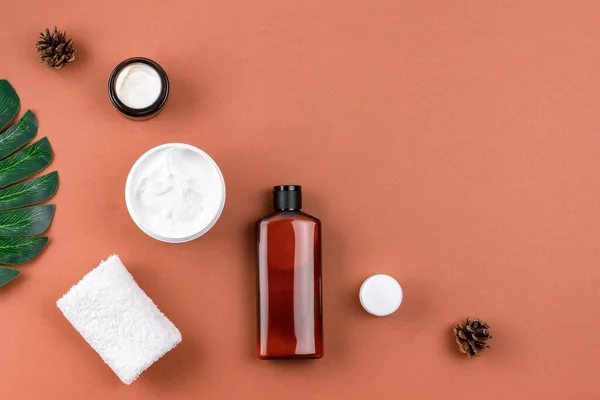 Wellness salon composition. Skincare products with natural ingredients on brown surface. Moisturizing facial mask cream in open jar, mockup bottle of lotion, towel. Spa concept. Copy space