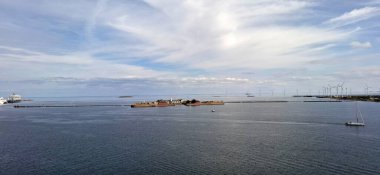 Danimarka sterbro sep 2. 2024 Bir ada, bir yelkenli tekne ve ufukta hafif bulutlu gökyüzü altında rüzgar türbinleri ile sakin bir deniz manzarası