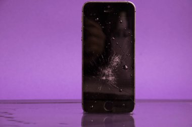Mor arka planda, su damlalarında siyah, kırılmış bir telefon yatıyor.