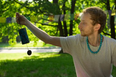 Buddhist man holds in his hands a Buddhist black and blue bell on a background of nature