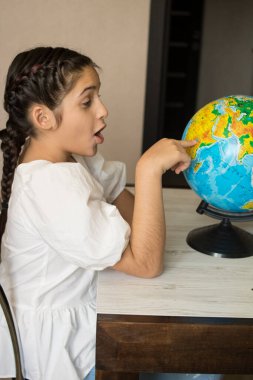 Little beautiful girl in a white dress examines and studies the globe. Good for billboards, posters, flyers. clipart