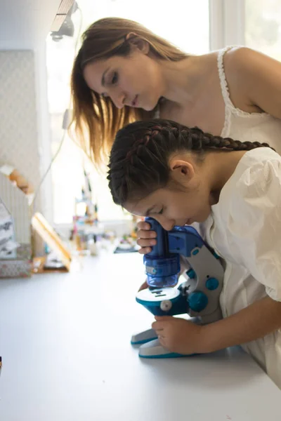 Mom and daughter look through a blue microscope. Good for banners, posters, flyers.