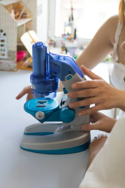 Mom and daughter look through a blue microscope, study biology and bacteria at home. Suitable for training centers, leaflets, brochures, banners.