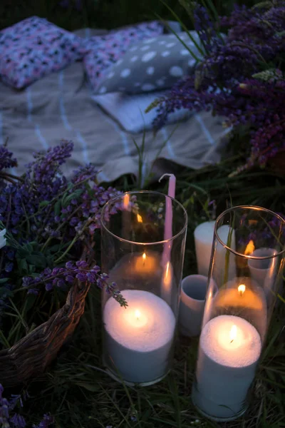 Beautiful candles in transparent glass goblets and purple lupins in a wooden basket are standing on green grass. Good for banners, posters, flyers.