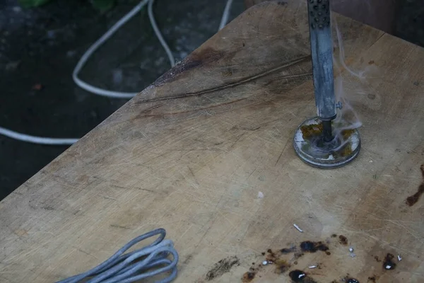 An experienced guy solders a tin with an old soldering iron on an old dirty light table
