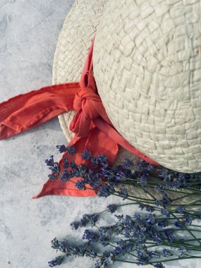 Kırmızı kurdeleli ve lavantalı parlak yaz şapkası gri bir masada yatıyor.