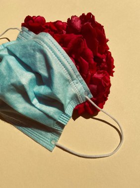 Tıbbi mavi koruyucu maske ve sarı arka planda kırmızı güller. Salgın, virüs, koronavirüs, covid-19.