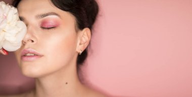 Pembe makyajlı, elinde şakayık, pembe arka planda bir kız.