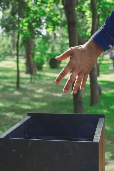 青いシャツの男がゴミ箱にゴミを投げ込んだ — ストック写真