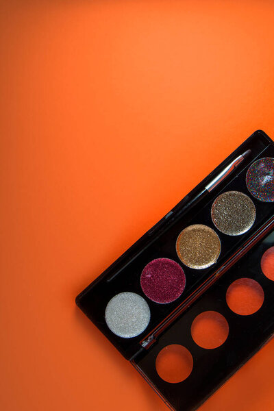 Palette with eye shadow on orange background