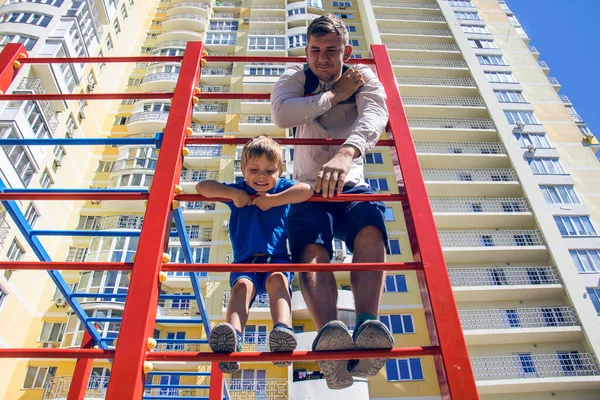 赤の子供のスポーツクライミングフレーム上のお父さんと息子 ロイヤリティフリーのストック写真