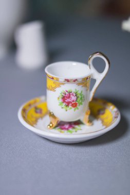 Gri masada küçük beyaz ve sarı fincan ve tabak.