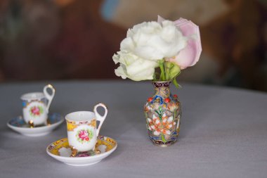 Çay seti ve vazo, gri masada beyaz ve pembe güller.