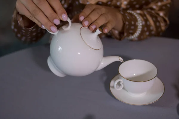 女孩把茶从一个白茶壶倒入一个白杯子 — 图库照片