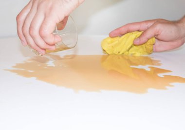 Adam beyaz masayı dökülen çaydan sarı bir bezle siliyor.