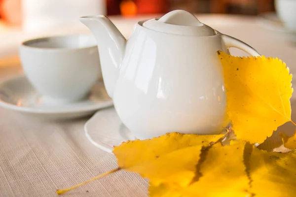 淡淡的桌上放着白茶壶和黄秋的叶子 — 图库照片