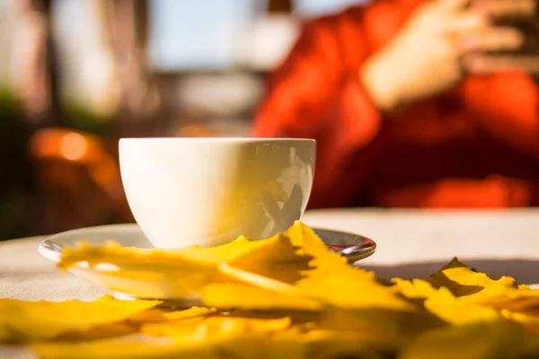 白いテーブルの上にお茶と黄色の秋の葉を持つ白いカップ ロイヤリティフリーのストック画像